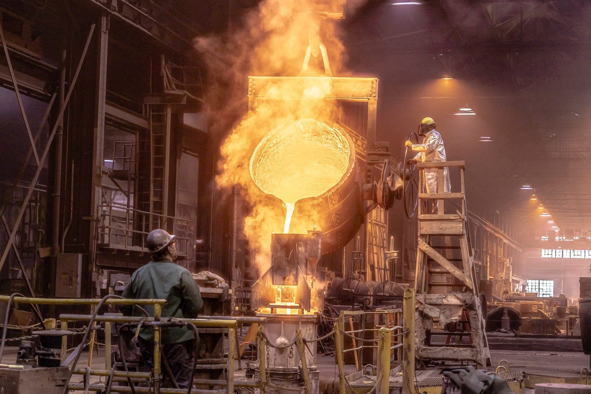 A ladle pouring molten metal while a roller watches from the floor